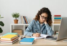 Pessoa estudando inglês com livros e computador, cercada de materiais coloridos e uma atmosfera inspiradora.