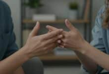 Close-up de duas pessoas conversando em um ambiente de terapia, com foco nas mãos gesticulando para simbolizar apoio e escuta na saúde mental.