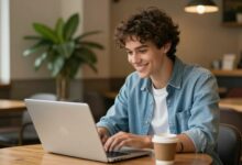 Um jovem sorrindo enquanto trabalha em um laptop em um café aconchegante, com uma planta ao lado, simbolizando um trabalho de férias flexível e moderno.