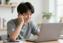 Um jovem estudante sorrindo, sentado em um café com um laptop, equilibrando trabalho e lazer durante as férias.