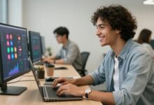Uma pessoa sorrindo enquanto trabalha em um notebook com gráficos de redes sociais na tela, em um ambiente de escritório moderno e iluminado.