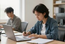 Uma pessoa sentada em uma mesa de trabalho organizada e iluminada, olhando concentradamente para um caderno, com um laptop fechado ao lado, simbolizando foco e a eliminação de distrações digitais.